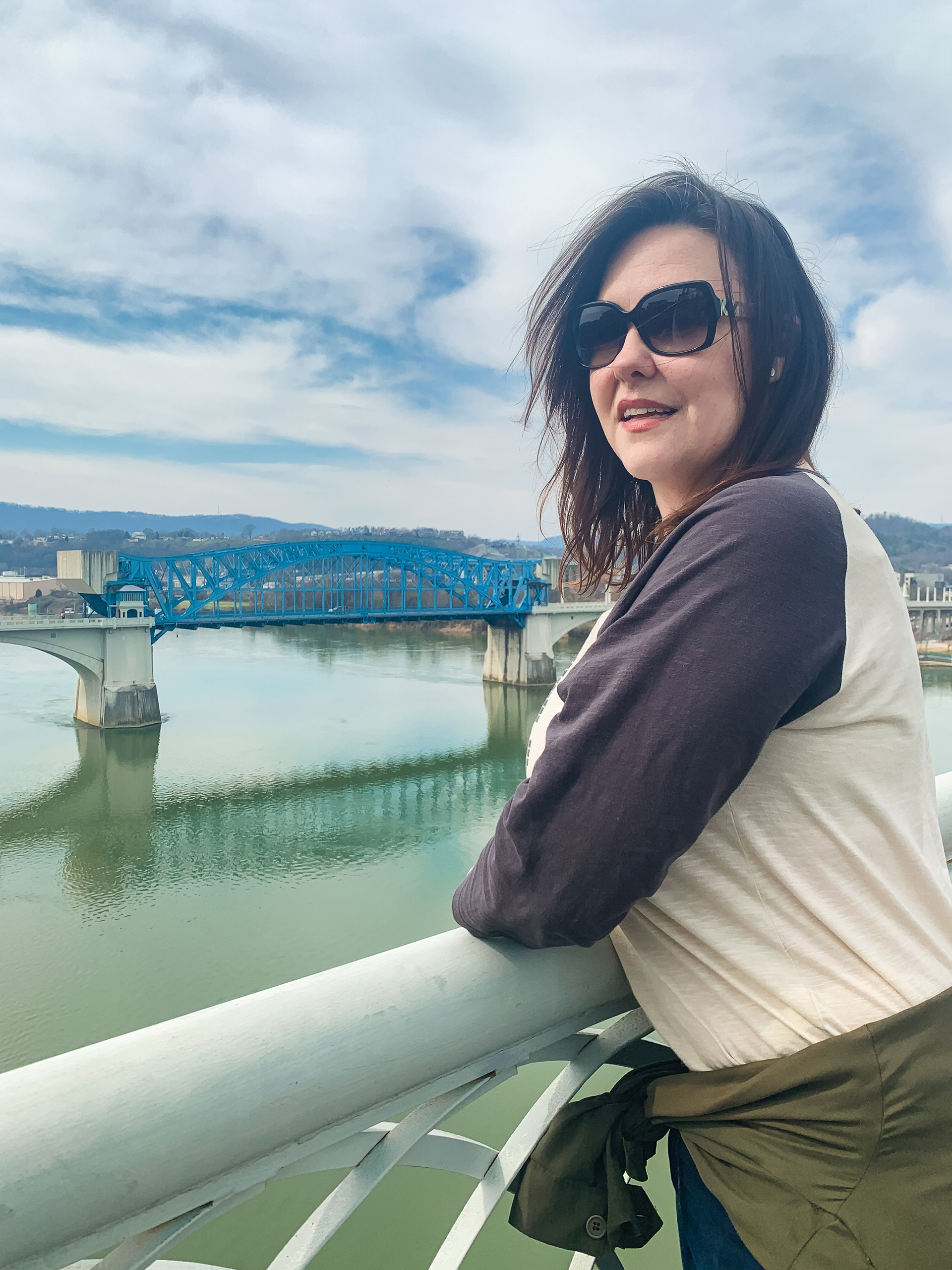 a woman looks out over a river from a bridge with another bridge in the background