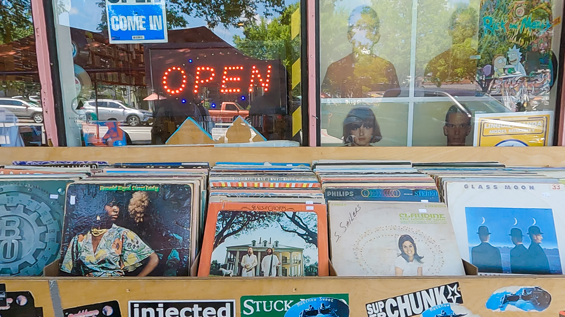 crates of vinyl records and a neon open sign outside a record store window